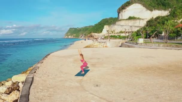 Hava manzaralı kadın, okyanus manzaralı plajda yoga egzersizleri yapıyor ve esniyor. — Stok video