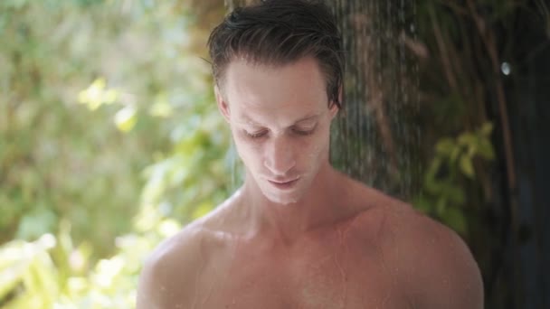 Portrait of sexy man takes refreshing tropical shower, greneery on background — Stock Video