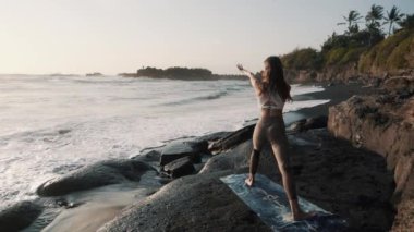 Arka manzara, yoga yapan kız mindere uzanıyor, okyanus kıyısındaki siyah kum plajı.