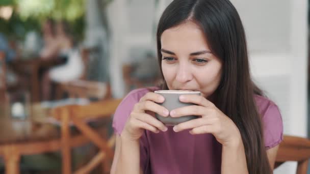 Портрет красивой женщины, пьющей горячий напиток из чашки в кафе и улыбающейся — стоковое видео