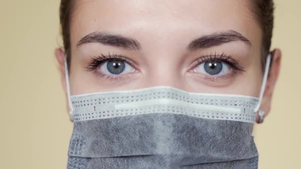 Close up rosto de jovem mulher em máscara médica protetora olhando para a câmera — Vídeo de Stock