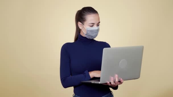 Porträtt av brunett kvinna i skyddande medicinsk mask använder laptop för arbete — Stockvideo