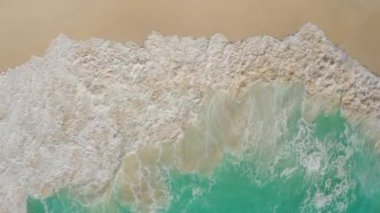 Gök mavisi suyu ve köpüren okyanus dalgalarıyla dolu beyaz kumsalın drone görüntüleri.