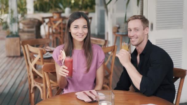 Coppia felice in caffè, uomo e donna bere succhi di frutta freschi, guardare la fotocamera, sorridere — Video Stock