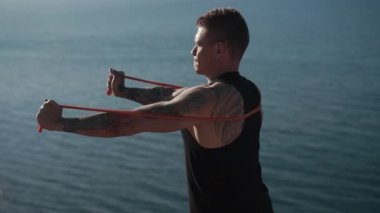 Dövme trenleri olan kaslı bir adam. Açık deniz manzaralı lastik bantlı.