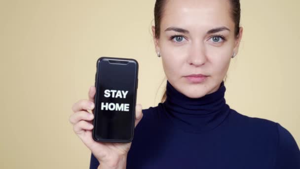 Retrato de chica morena muestra teléfono con inscripción permanecer en casa durante la epidemia — Vídeos de Stock