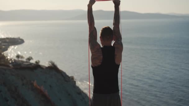 Вид сзади, мужчина с татуировкой мышцы, тренирующийся с эластичными повязками на открытом воздухе — стоковое видео
