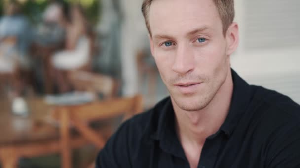 Портрет красивого чоловіка, що сидить у кафе і дивиться на камеру, посміхається — стокове відео