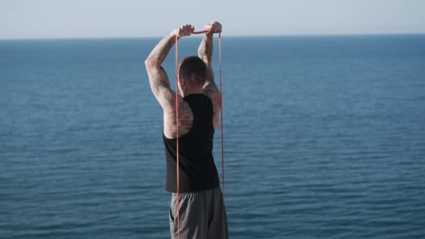 Вид сзади на мускулистые татуированные тренировки спортсмена с эластичными полосами на открытом воздухе — стоковое видео