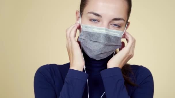 Молодая женщина слушает музыку в наушниках и танцует в маске медицинской защиты — стоковое видео