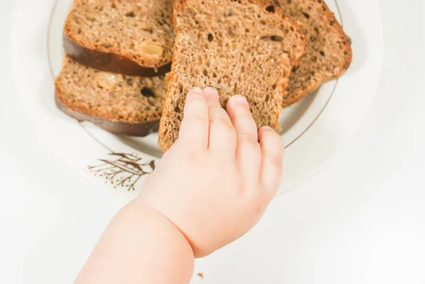 Children's hand takes a slice of fresh bread with spices, raisins and nuts — Stock Photo, Image