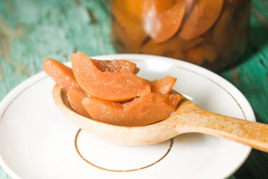 Güzel kokulu taze tatlı portakal reçeli olgun sulu armut üzerinden. Dilimlenmiş yeşil ahşap arka plan üzerinde beyaz bir plaka üzerinde bir tahta kaşık, armut ve armut suyu