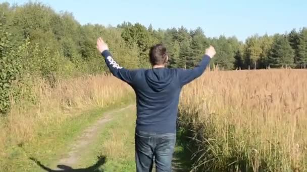Joven caminando y levantando las manos en el campo — Vídeos de Stock