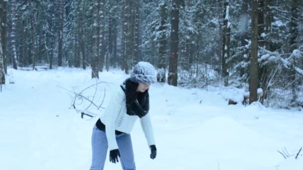 Grappig speels meisje gooien sneeuwbal rechtstreeks naar camera, witte spatten vliegen rond. Bedriegt rond in de sneeuw en de wandelingen in het bos. Sneeuw langzaam naar beneden vallen. — Stockvideo