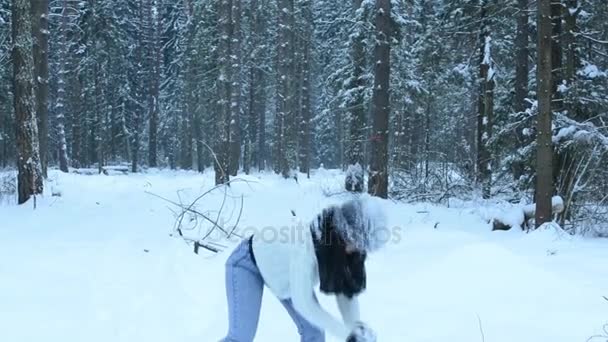 Chica divertida juguetona lanzar bola de nieve directamente a la cámara, salpicaduras blancas vuelan alrededor. Haciendo el tonto en la nieve y caminando por el bosque. La nieve cae lentamente . — Vídeos de Stock