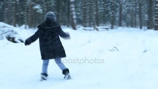 Chica divertida juguetona lanzar bola de nieve directamente a la cámara, salpicaduras blancas vuelan alrededor. Haciendo el tonto en la nieve y caminando por el bosque. La nieve cae lentamente . — Vídeo de stock