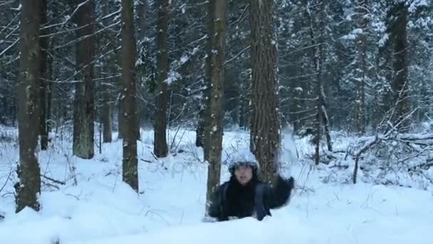 Grappig speels meisje gooien sneeuwbal rechtstreeks naar camera, witte spatten vliegen rond. Bedriegt rond in de sneeuw en de wandelingen in het bos. Sneeuw langzaam naar beneden vallen. — Stockvideo