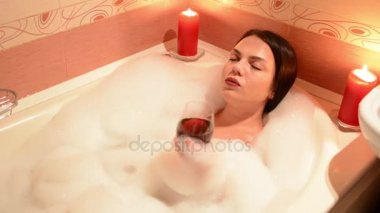 Bir kadeh şarap ile köpük banyosu alarak güzel kız. Bir büyük beyaz banyo ve yüzünde sevinç. gevşeme kavramı