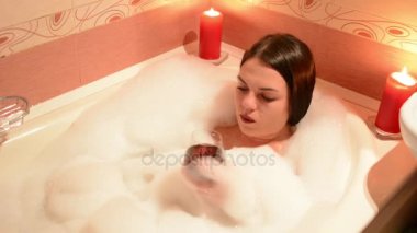 Bir kadeh şarap ile köpük banyosu alarak güzel kız. Bir büyük beyaz banyo ve yüzünde sevinç. gevşeme kavramı