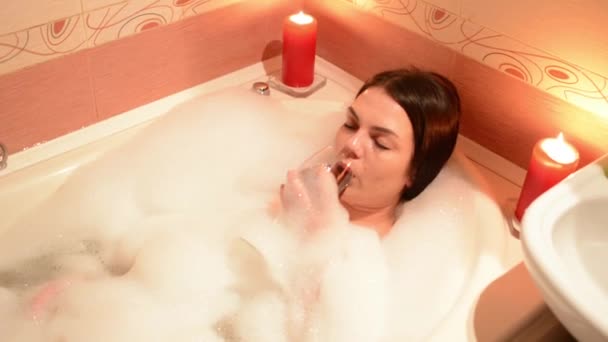 泡風呂にワインのグラスと美しい少女 大きな白いお風呂と彼の顔に喜び リラクゼーション コンセプト — ストック動画
