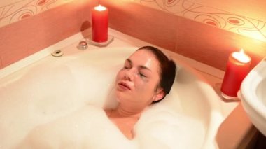 Güzel genç kadın rahatlatıcı romantik mum arka plan tarafından jakuzi küveti spa resort. Köpük, çığlıkları ve gülüyor dalmış.