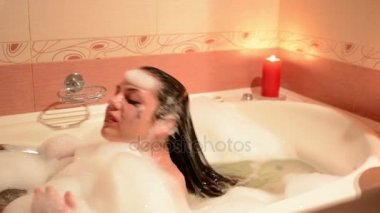 Güzel genç kadın rahatlatıcı romantik mum arka plan tarafından jakuzi küveti spa resort. Köpük, çığlıkları ve gülüyor dalmış.