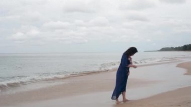 Plajda çiçekli mavi elbiseli boyunda esmer yürür