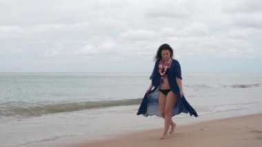 Plajda çiçekli mavi elbiseli boyunda esmer yürür