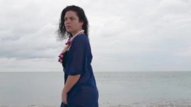 Plajda çiçekli mavi elbiseli boyunda esmer yürür