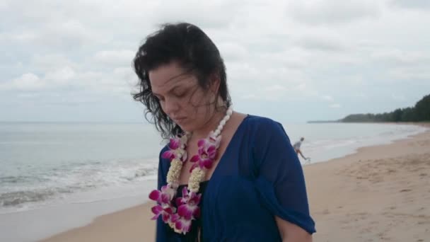 黑发漫步在沙滩上 穿着蓝色的连衣裙 脖子上有花 — 图库视频影像