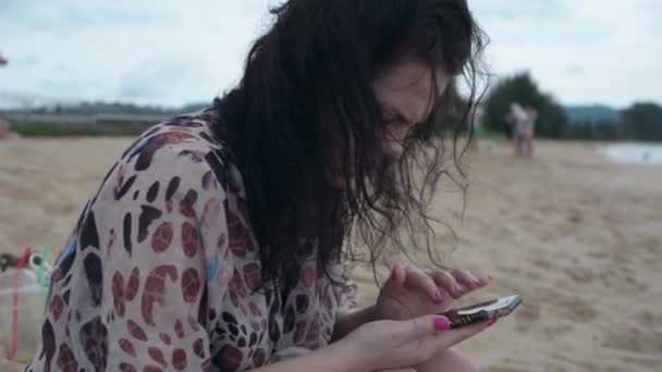 黑发女孩坐在海滩上用电话 — 图库视频影像