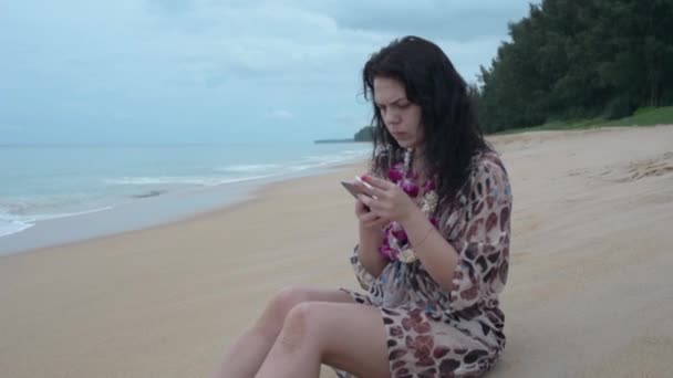 黑头发的女孩坐在海滩上用电话 女孩抽烟 — 图库视频影像