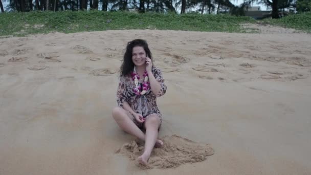 黑头发的女孩坐在海滩上用电话 女孩抽烟 — 图库视频影像