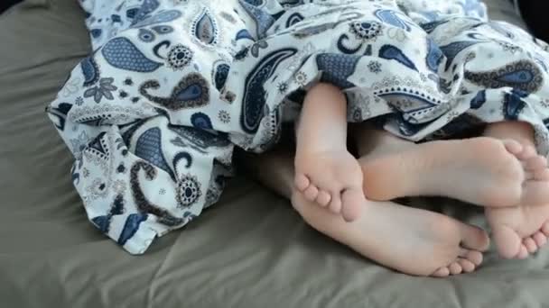 特写的美丽和爱对年轻夫妇拥抱并建立起他们的脚彼此在毯子下面同时醒来躺在床上在早上 — 图库视频影像