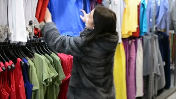 Feliz atraente jovem mulher fazendo compras no shopping comprando roupas escolhendo camisetas. Conceito de Shopaholismo de Consumismo — Vídeo de Stock