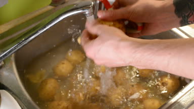 Lavaboya su ile bir bıçakla peeling ham patates erkek eller