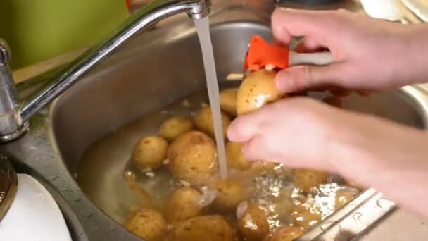 Mãos masculinas descascando batatas cruas com uma faca na pia com água — Vídeo de Stock