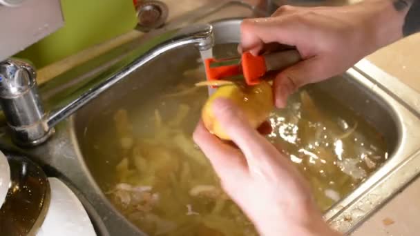 男性は水で流しにナイフで剥離生のジャガイモを手します — ストック動画