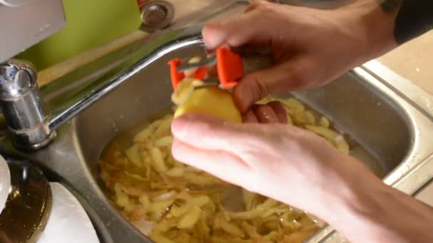 男性は水で流しにナイフで剥離生のジャガイモを手します — ストック動画
