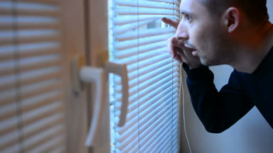 Perdeleri sokağa pencereden dışarı bakarak, casusluk adam. şüpheli