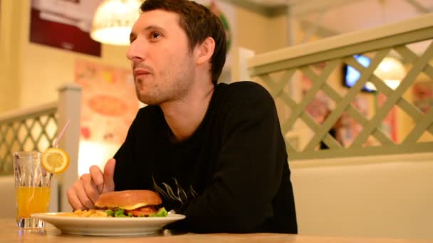 Um homem tem um hambúrguer em um restaurante e bebe limonada — Vídeo de Stock