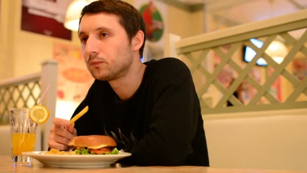 Un homme a un hamburger dans un restaurant et boit de la limonade — Video