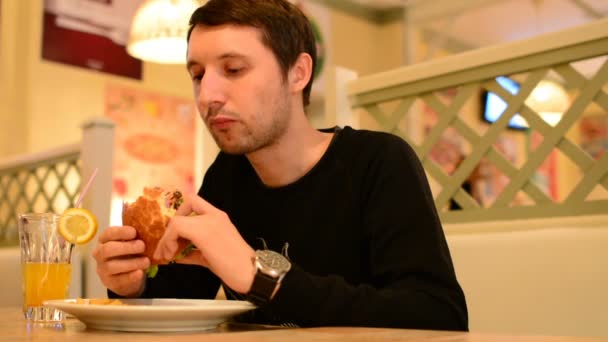 Un homme a un hamburger dans un restaurant et boit de la limonade — Video