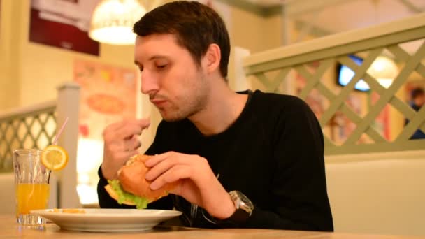 Un hombre tiene una hamburguesa en un restaurante y bebe limonada — Vídeos de Stock