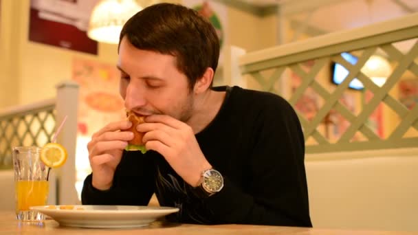 Un uomo ha un hamburger in un ristorante e beve limonata — Video Stock