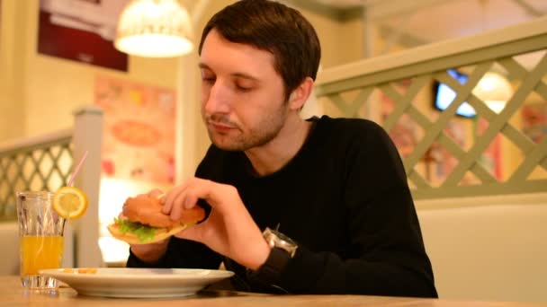 Een man heeft een hamburger in een restaurant en limonade drinken — Stockvideo