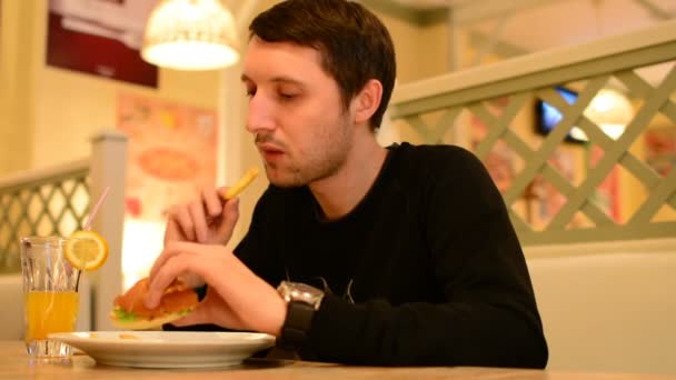 Un homme a un hamburger dans un restaurant et boit de la limonade — Video