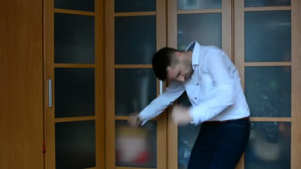 Молодой человек танцует дома против шкафа — стоковое видео