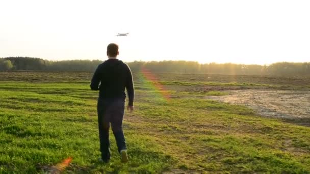 Молодий чоловік контролює безпілотник у полі на заході сонця . — стокове відео