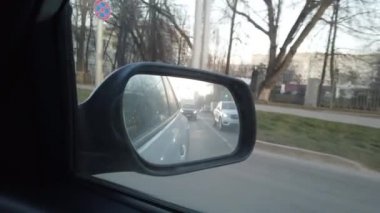 Dikiz aynasından arabanın görüntüsü görünüyor. Yoğun şehir sokaklarında araba sürüyorum..